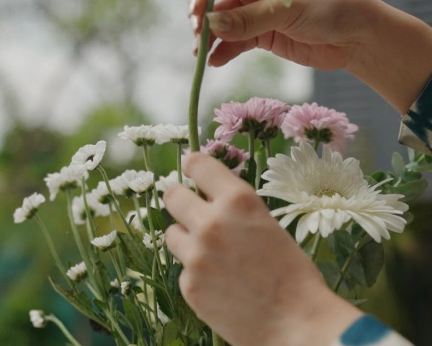 Person arranging flowers in a clear vase outdoors